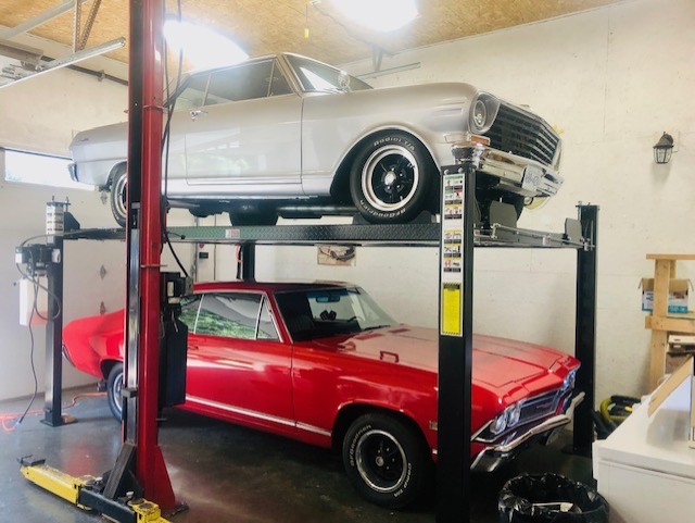 Two classic Chevrolets stacked on an Atlas PH8S four-post parking lift in a home garage
